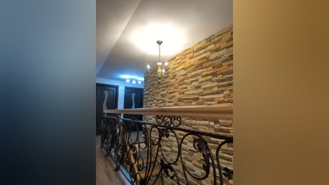 Media: Video of a modern interior staircase with a rustic stone accent wall, wrought iron railing, and a chandelier.