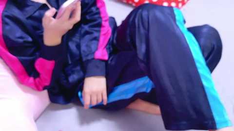 Media: Video of a person lounging on a couch, wearing a navy blue tracksuit with pink and blue stripes, holding a book, surrounded by a red polka-dotted cushion.