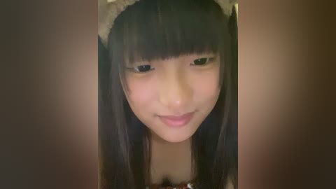 Media: A close-up video of a young Asian girl with straight black hair and bangs, wearing a beige headband, against a blurred, warm-toned background.