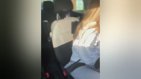 Media: Video of a car interior showing the backseat. A woman with long blonde hair, wearing a white jacket, is seated in the foreground. A man with a black shirt and dark hair sits behind her.