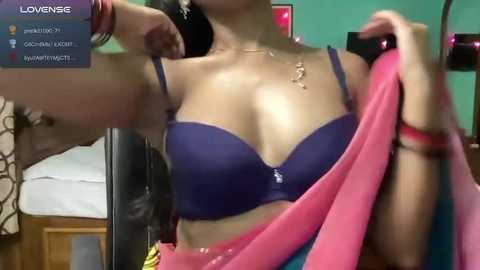 Media: A video of a woman in a purple bra, pink and blue sari, and red bangles, taken indoors, showing her cleavage and part of her face.