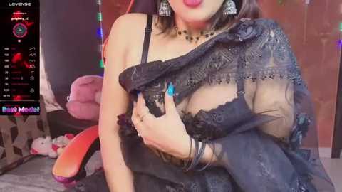 Media: A video of a curvy woman in a black lace bra, wearing a sheer black sari, with a pink gaming chair in the background.