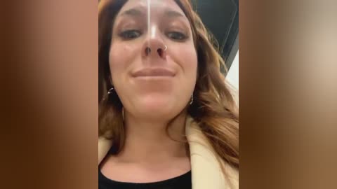 Media: Video of a smiling woman with light skin, long auburn hair, wearing a nose ring and hoop earrings, captured in a selfie with her face partially obscured by another person's hands.