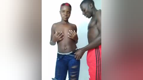 Media: Video of two African-American men: a shirtless man with red hair and blue jeans, and a man in red Adidas pants, standing in a minimalistic room.