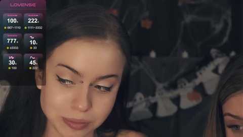 Media: Video of a close-up of a young woman with dark hair, wearing black makeup and a black dress, looking down with a contemplative expression.