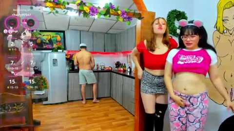 Media: A video of a modern kitchen with two women in anime-inspired costumes, one with a pink crop top and the other in a red crop top, standing near a shirtless man.