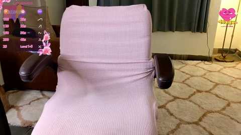 Media: A video of a beige recliner chair with a pink ribbed fabric cover, set against a cream carpet with a floral pattern, in a room with dark curtains and a white wall.