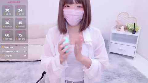 Media: Video of an Asian woman in a white lab coat and mask, holding a glowing green orb, in a minimalistic, light-toned room.