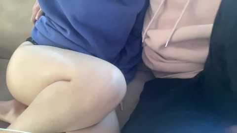 Media: Video of a person's upper body, focusing on their large, round buttocks clad in tight, beige shorts. They are sitting on a beige couch, partially covered by a blue shirt and a pink hoodie.