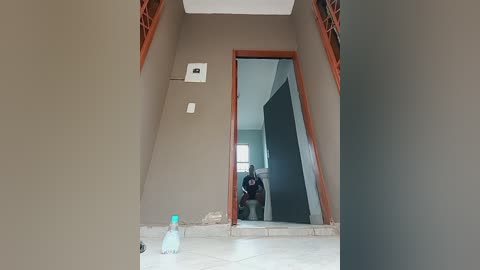 Media: Video of a beige hallway with a large mirror, reflecting a person in a dark shirt. The mirror has a wavy, damaged edge. A clear water bottle is on the floor.