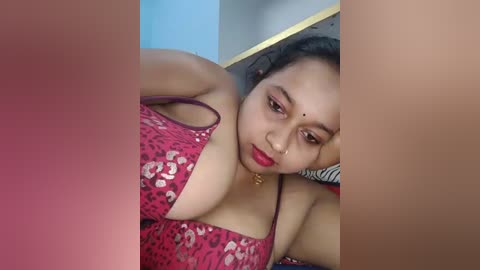 Media: A video of a South Asian woman with medium skin tone, wearing a red and white leopard print top, lying on her side, with her left arm propped up.