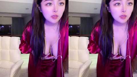 Media: Video of an Asian woman with long dark hair, wearing a low-cut red satin robe, sitting on a white leather couch in a modern living room.