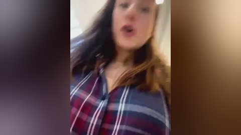 Media: A blurred video of a woman with shoulder-length, dark hair and a plaid shirt, mouth open as if mid-sentence. The background is out of focus.