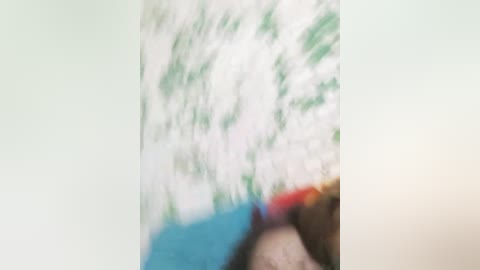 Media: The image is a blurred video featuring a close-up of a person's face. The background is indistinct, with green and white textures. The person's skin tone is unclear, and their facial features are obscured. The overall image appears out of focus.