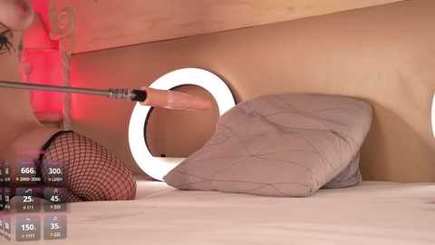 Media: Video of a woman with a large dildo, wearing black fishnet stockings, lying on a bed with a round light above.