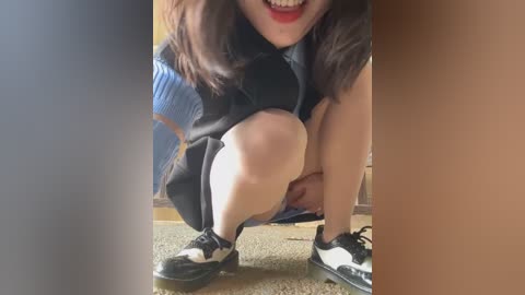 Media: Video of a woman squatting, wearing a black dress, blue sweater, and black and white shoes. She has fair skin, dark hair, and red lipstick, smiling.