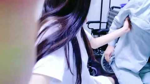 Media: Video of a woman with long, dark hair wearing a white t-shirt, pulling up a man's light blue shirt in a salon setting.