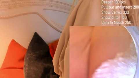 Media: Video of a woman wearing a beige coat, pulling down the zipper, revealing her bare back and buttocks, set in a cozy bedroom with orange and black pillows.