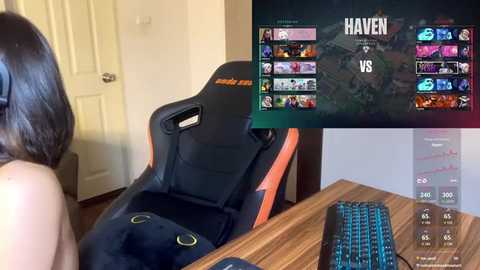 Media: Video of a gamer sitting in a black and orange gaming chair, wearing headphones, with a wooden desk and keyboard.