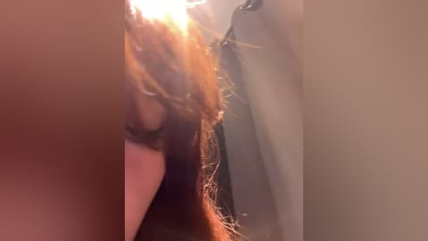 Media: A close-up video of a woman's face with long, wavy, auburn hair, partially in shadow, highlighting the texture and movement of her hair.