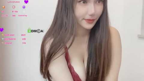 Media: Video of a young Asian woman with long, straight, dark brown hair and fair skin, wearing a red lace bra, smiling. Background is a plain white wall.