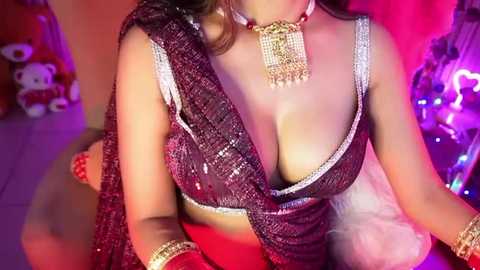 Media: Video of a South Asian woman with fair skin, wearing a revealing, sequined black sari, gold necklace, and matching earrings, against a colorful, festive background with lights.