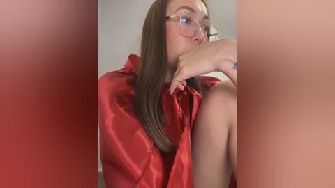 Media: A video of a fair-skinned woman with long, straight brown hair, wearing glasses, a red satin robe, and a contemplative expression, against a blurred red background.