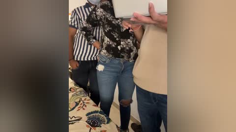 Media: Video of two men, one in a striped shirt and the other in a floral top, standing in a beige room. The man on the right wears a beige sweater and has a hand raised.