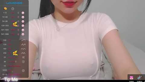 Media: Video of an Asian woman with medium breasts, wearing a white t-shirt, taken in a bedroom setting. The image is captured from a smartphone, with a live stream overlay showing stats and emojis.