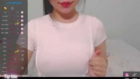 Media: A video of an East Asian woman with long black hair and red lipstick, wearing a sheer white top that reveals her large breasts. The background is a white room with a bed.