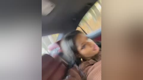 Media: A blurry video captures a young woman with dark skin and medium-length hair in a car, her eyes closed, possibly asleep, wearing a light pink sweater.