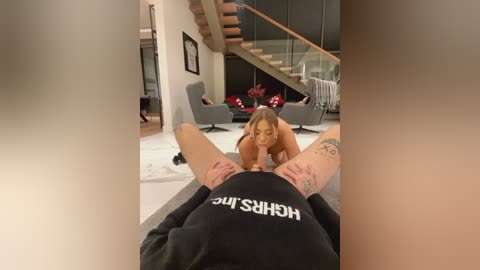 Media: Video of a woman performing oral sex on a man lying on a couch in a modern living room with a spiral staircase and glass walls.