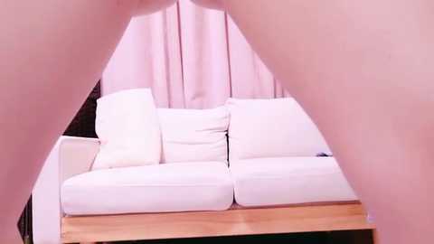 Media: A video of a person lying on a white sofa with a pink curtain backdrop, taken from a low-angle perspective. The image is bright and clean, focusing on the soft textures of the sofa and curtain.