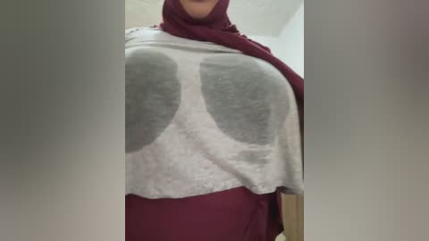 Media: Video of a person wearing a maroon hijab, a white T-shirt with large, gray, cartoonish lungs graphic, and a maroon shirt underneath. The background is a plain, beige indoor setting.