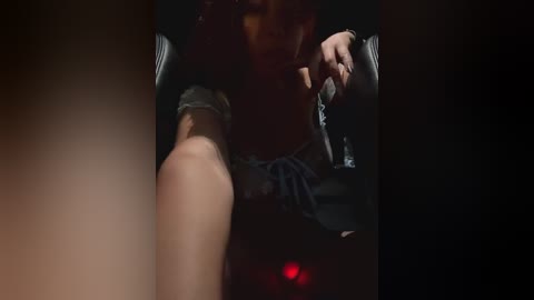 Media: A dimly lit, close-up video captures a woman's arm in a black sleeve, with her hand holding a smartphone. Her face is partially obscured, and the background is dark and blurry.