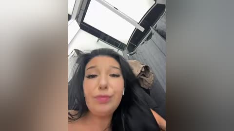 Media: A video of a woman with long, dark hair and light skin, wearing headphones, lying on a bed with grey sheets, inside a modern, well-lit room with a skylight.