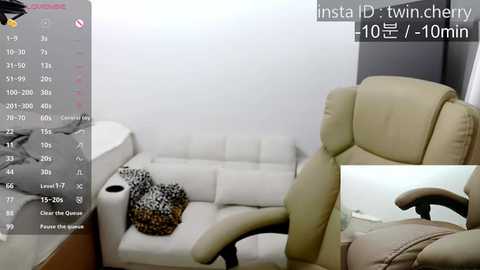 Media: A video of a minimalist, beige upholstered office chair positioned in a corner of a white-walled room with a bed and a leopard-print blanket on the left.