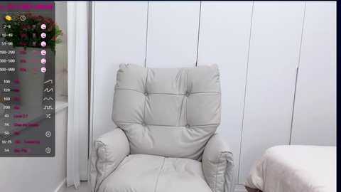 Media: Video of a modern, cream-colored, tufted armchair in a minimalist bedroom with white walls and a bed visible in the background. The image includes a smartphone screen with social media notifications on the left side.