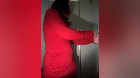 Media: Video of a woman with long brown hair, wearing a red dress, pressing against a door, with red and white lights creating a dramatic effect.