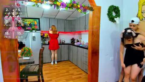 Media: Video of a modern kitchen with a woman in a red dress, another woman in a black dress, and a man in a black shirt, all looking at a TV.