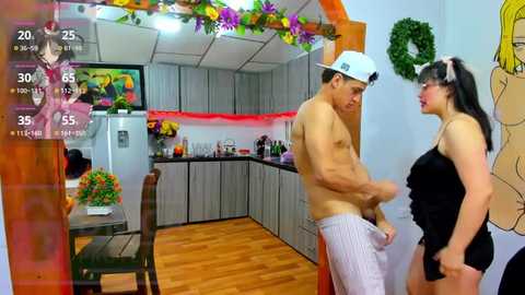 Media: A video of a shirtless man in striped pajama pants and a woman in a black top, standing in a vibrant kitchen adorned with cartoon decorations, including a TV screen showing a character.