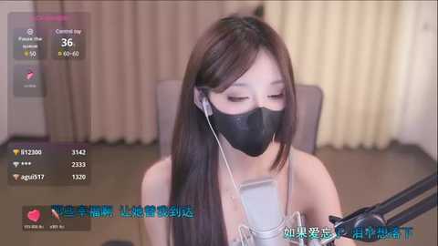 Media: A video of an Asian woman with long brown hair, wearing a black mask, listening to headphones, sitting at a desk in a modern room with beige curtains.