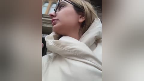 Media: A video of a woman with light skin, wearing a white hoodie and black glasses, looking upward in a dimly lit room with blurred, indistinct background.