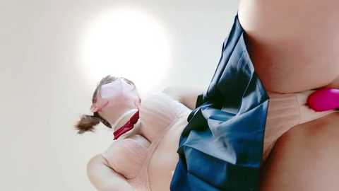 Media: Video of a woman in a white shirt and red tie, with a blue skirt, tied up and gagged, against a white wall.