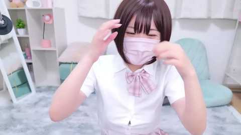 Media: A video of an Asian woman with straight, dark brown hair, wearing a white shirt, pink bow, and pink mask, adjusting her mask indoors with soft, pastel decor in the background.