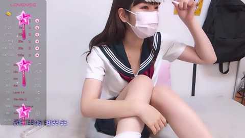 Media: Video of an East Asian woman with long black hair, wearing a white sailor schoolgirl uniform and a pink face mask, sitting on a white floor, brushing her hair.