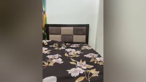 Media: Video of a modern, minimalist bedroom with a dark brown, tufted headboard. The bed features a black and white floral duvet. The walls are white, and a colorful abstract painting is partially visible in the background.