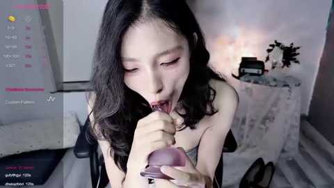 Media: Video of an East Asian woman with long black hair, fair skin, and a slender physique, performing fellatio on a man. The background features a minimalist room with white walls and a cluttered desk.