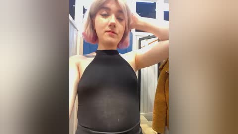 Media: A video of a young woman with light skin and shoulder-length pink hair, wearing a tight black bodysuit that reveals her pregnant belly, standing in a narrow, white-walled hallway.