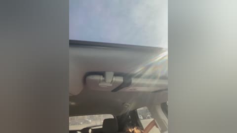 Media: Video of a car's interior showing a partially open sunroof with a rainbow effect, revealing a clear blue sky. The car's roof is metallic, and the sunroof handle is visible. The image is slightly blurred, giving a sense of motion.